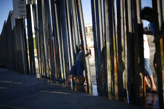 A boy tries to touch the sand on the other side of a the wall separating Mexico and the United States in Imperial Beach, California November 5, 2010. A fence of metal pillars marks the westernmost edge of the nearly 2,000 mile border between the United States and Mexico, which spans five states across the southern U.S. REUTERS/Eric Thayer