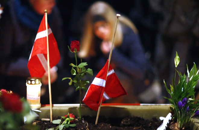 Copenhagen, Denmark Danish flags are placed next to flowers as people gather for a memorial service held for those killed on Saturday by a 22-year-old gunman, in Copenhagen February 16, 2015. Danish police said on Monday they had charged two people with aiding the man suspected of shooting dead two people in attacks on a synagogue and an event promoting free speech in Copenhagen at the weekend. The shootings, which Danish Prime Minister Helle Thorning-Schmidt called acts of terrorism, sent shockwaves through Denmark and have been compared to the January attacks in Paris by Islamist militants that killed 17. REUTERS/Hannibal Hanschke