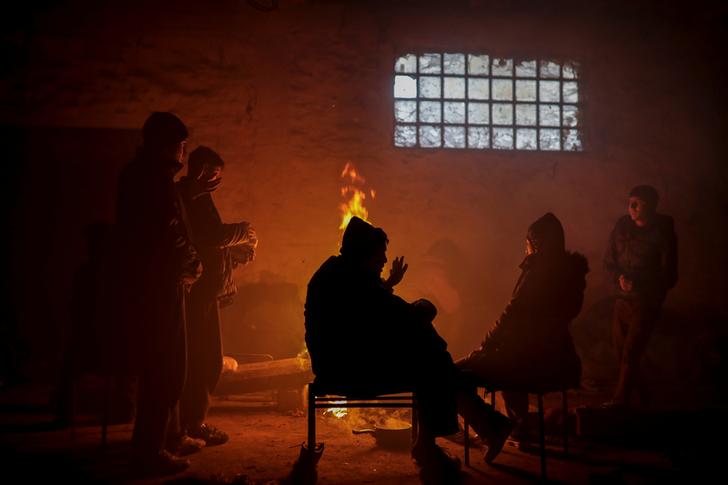 Migranti si scaldano davanti al fuoco dentro un magazzino abbandonato. Belgrado, Serbia, REUTERS/Marko Djurica