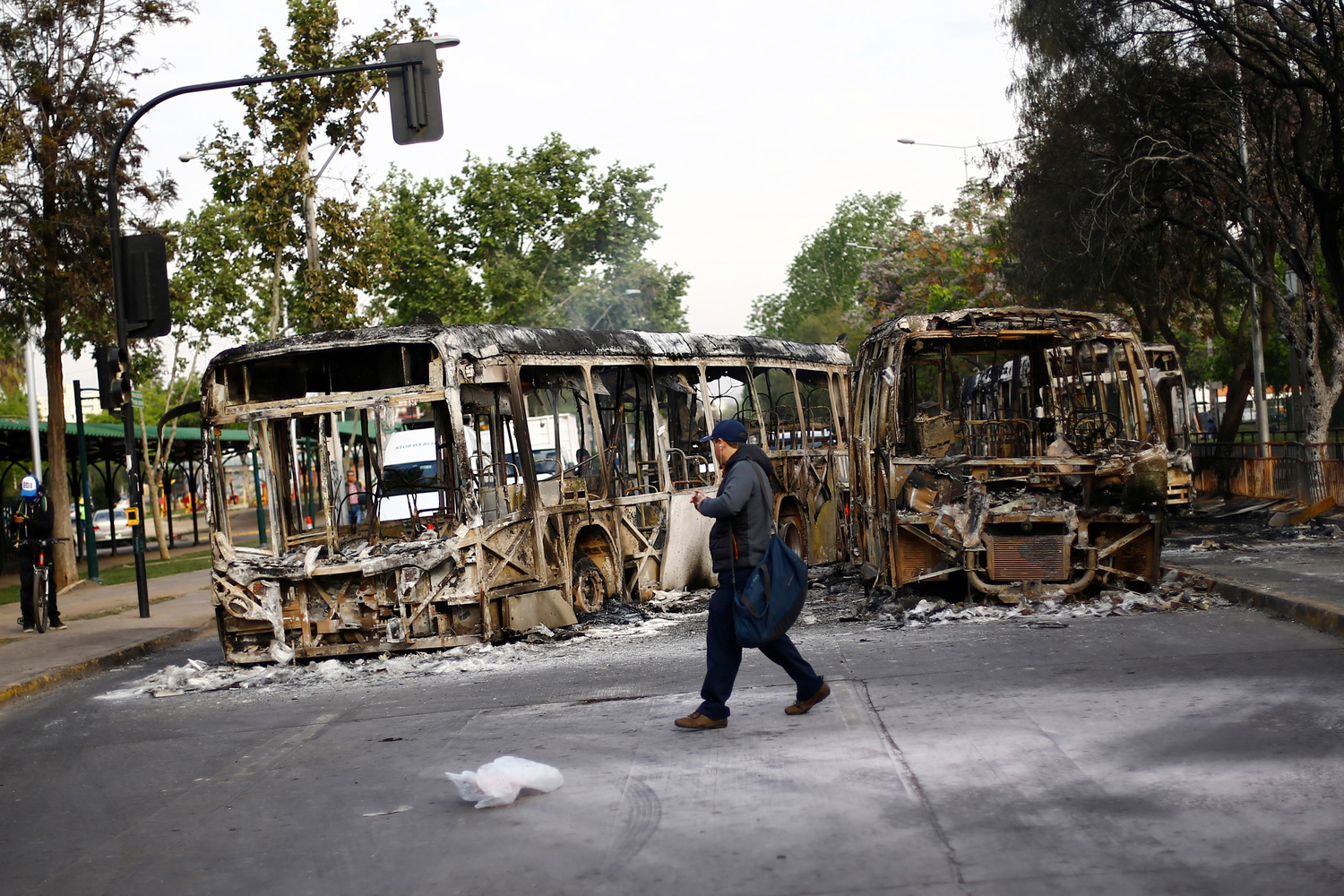 Un uomo cammina di fronte a due autobus bruciati dopo una protesta contro l'aumento dei prezzi dei biglietti della metropolitana a Santiago, Cile, 19 ottobre 2019. REUTERS/Edgard Garrido