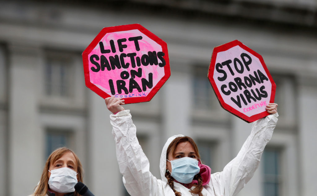 Una donna tiene manifesti durante una protesta contro le sanzioni all'Iran che bloccano il materiale sanitario necessario a curare il coronavirus