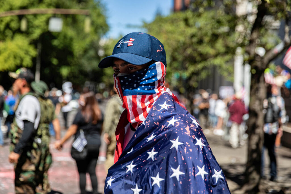 Usa 2020: gli ultimi mesi della campagna elettorale. Un uomo indossa la bandiera americana durante la manifestazione a Portland, Oregon, Stati Uniti, 22 agosto 2020. REUTERS/Maranie Staab